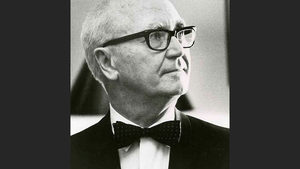 Historical black and white headshot of white man with black rimmed glasses wearing a suite and bow tie.