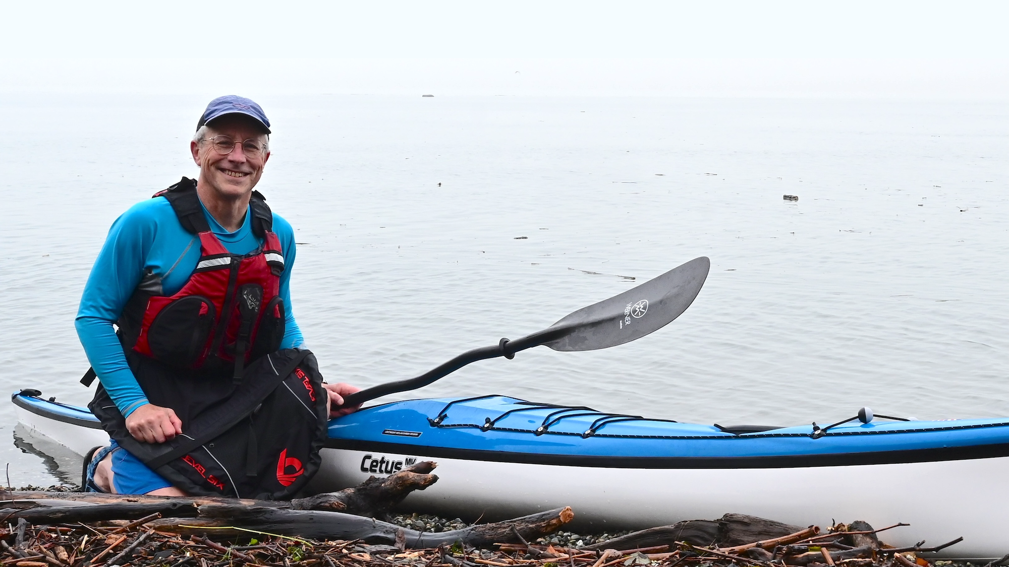 Person kneeling next to kayak on a beach.