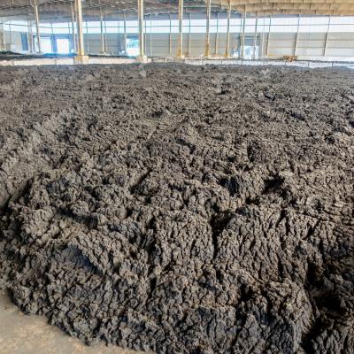 A large indoor facility containing a wide expanse of dark, thick, biosolids spread across the floor beneath a roof structure.