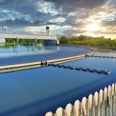 Circular wastewater clarifier with mechanical equipment under cloudy sky at sunset