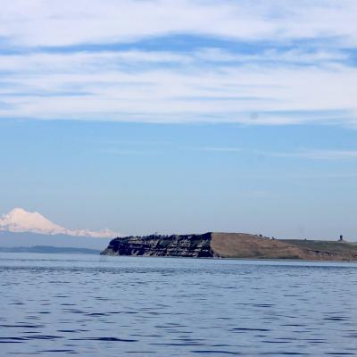 View of small treeless island surrounded by water, snow covered mountain in the background.