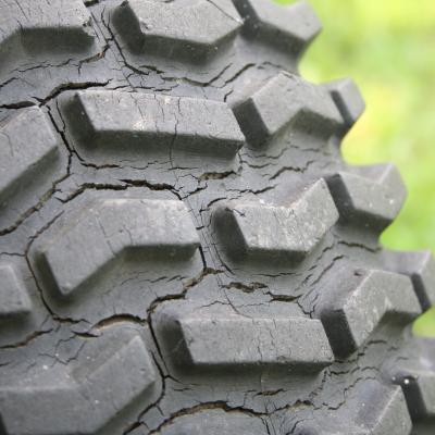Closeup of a weather-cracked tire tread against a green background.