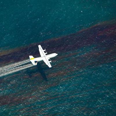 A plane releases chemical dispersant to break up an oil slick on the water surface below. Photo courtesy of the National Commission on the Deepwater Horizon Oil Spill and Offshore Drilling.