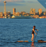 Person standing on a paddle board with the Seattle skyline in the background.