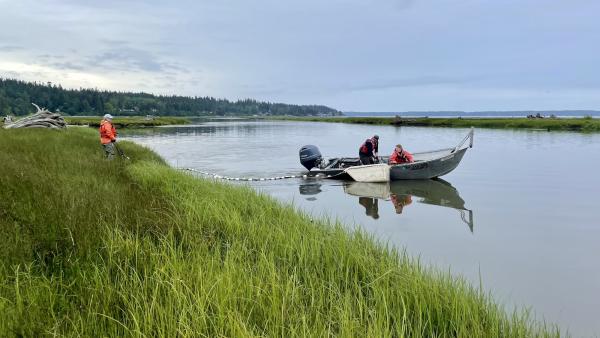 An open motor boat sitting in sill water as to people place a fishing net across the channel.