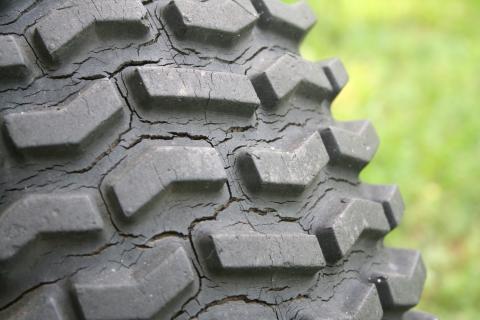 Closeup of a weather-cracked tire tread against a green background.