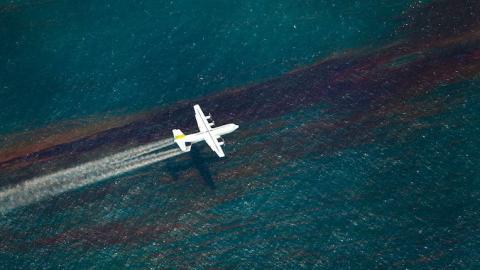 A plane releases chemical dispersant to break up an oil slick on the water surface below. Photo courtesy of the National Commission on the Deepwater Horizon Oil Spill and Offshore Drilling.