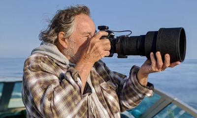 A man on a boat looking through a camera with a large lens.