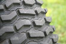 Closeup of a weather-cracked tire tread against a green background.