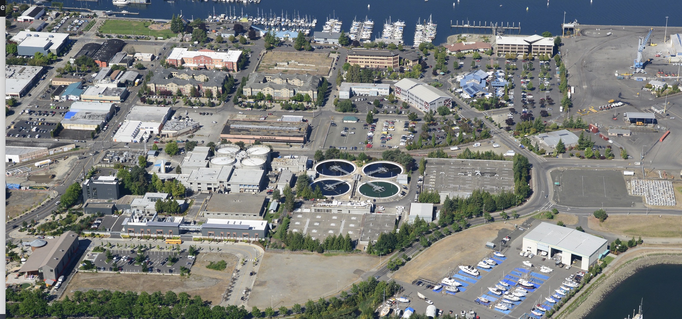 Olympia’s Budd Inlet Treatment Plant, center, is one of the few nitrogen-removing systems on Puget Sound. Photo: Washington Department of Ecology Aerial view of marina with boats, nearby water treatment plant with four circular tanks, surrounded by buildings, roads, and green space.