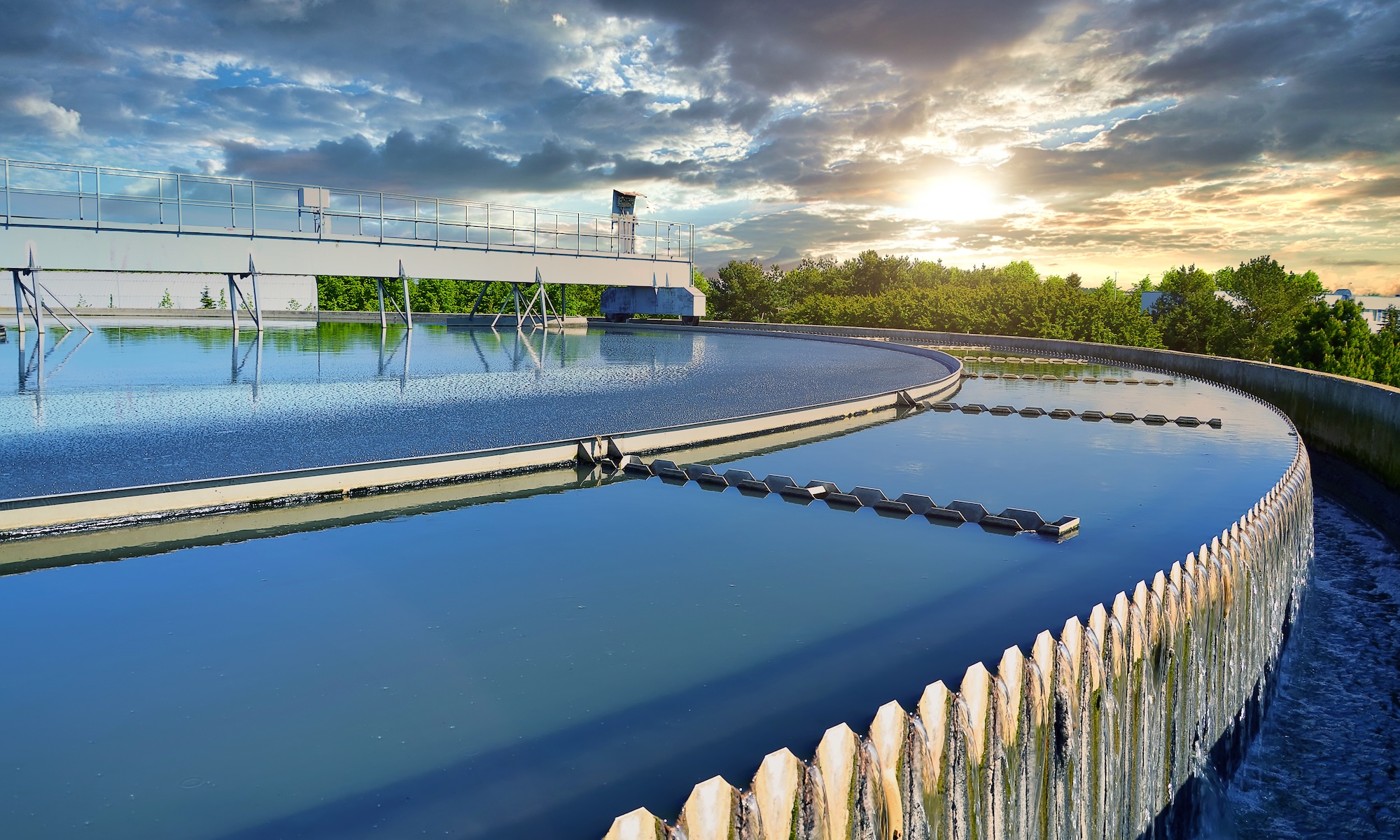 Circular wastewater clarifier with mechanical equipment under cloudy sky at sunset