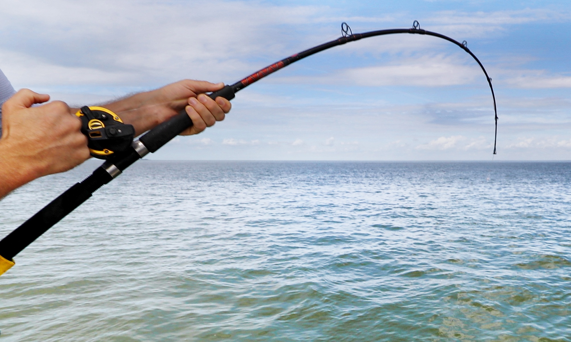 A pair of hands holding a fishing rod curving down toward open water. 