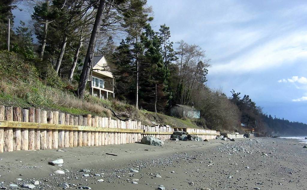 Timber pike seawall below a house along the shoreline.