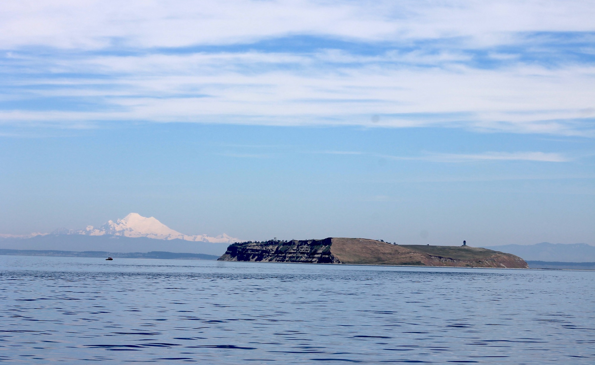 View of small treeless island surrounded by water, snow covered mountain in the background.